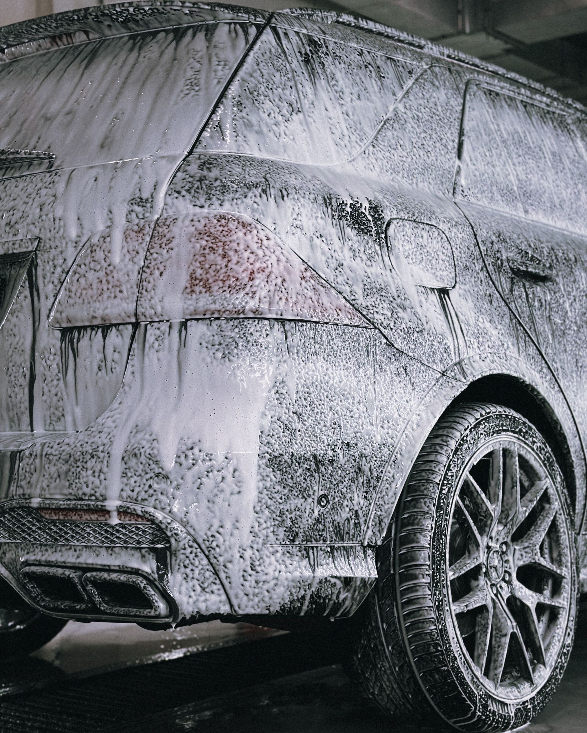 A premium SUV being cleaned with foamy soap in a detail car wash facility.