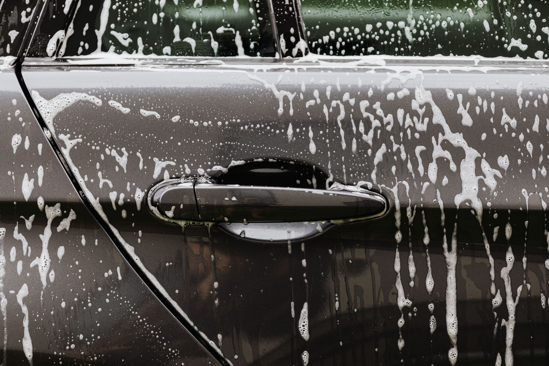 Detailed close-up of soap suds on a black car door during a wash, highlighting automotive care.